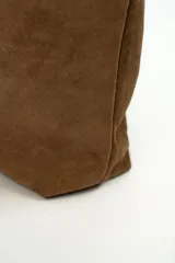 Bolso tipo shopper de gamuza marrón, con asa de hombro ajustable decorada con ojales metálicos plateados y hebilla lateral.