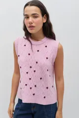 Chaleco de punto color celeste, con diseño de trenzas y pequeñas flores bordadas a mano en color marrón oscuro. Presenta cuello redondo y terminaciones acanaladas.