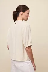 Blusa de manga corta color negro, con calce relajado, escote redondo con abertura y lazo para anudar. Presenta detalles de tablas horizontales en la parte superior que aportan textura al diseño.