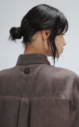 Camisa de corte oversize y mangas cortas, confeccionada en tela con efecto de teñido artesanal maltinto en tono gris. Presenta cuello clásico, cierre frontal con botones y costuras verticales decorativas en el frente.