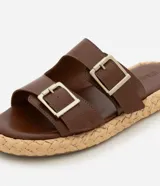 Sandalias marrones con dos tiras anchas con hebillas plateadas y suela plana con textura de rafia.
