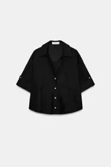 Camisa crop efecto denim color negro, con cuello solapa, escote en V, mangas cortas con trabilla y bolsillos frontales de parche. Cierre frontal con botones.