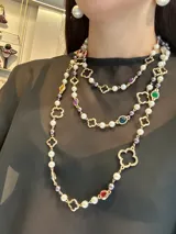 Collar largo de diseño versátil compuesto por una cadena de metal dorado con eslabones en forma de trébol, intercalados con perlas blancas, perlas grises y cuentas de cristal en tonos naranja, rojo y violeta.