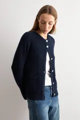 Chaqueta tejida de punto acanalado en color azul marino, con cuello redondo, cierre frontal de botones metálicos y dos bolsillos delanteros aplicados.