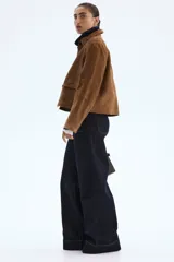 Pantalón de jean de tiro alto, color azul oscuro (índigo), con pierna ancha y corte cropped. Presenta bolsillos de parche grandes en la parte delantera y costuras en color ocre.