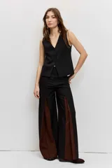 Pantalón sastrero de corte ancho y tiro alto, color negro con inserciones laterales en tono marrón que forman godets.