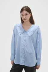 Camisa de algodón color celeste, con cuello grande tipo babero con volados, cierre frontal con botones y mangas largas con puños.
