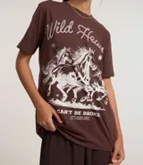 Remera de algodón color marrón, con cuello redondo, mangas cortas y estampado western de caballos con la frase 'Wild Heart' en color blanco.