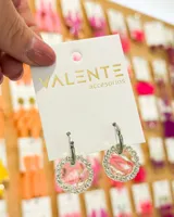 Aros colgantes plateados con forma circular, con borde de strass y centro con diseño abstracto en tonos rosados y blancos. El aro es de acero.
