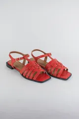 Sandalias de cuero color negro, de suela plana, con tiras entrelazadas en la capellada y tira ajustable en el talón con hebilla metálica.