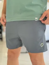 Short de baño gris liso, con diseño clásico y un pequeño parche circular con logo en la parte inferior de la pierna izquierda.