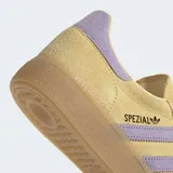 Championes Adidas modelo Handball Spezial, confeccionados en gamuza color amarillo con detalles en lila en las bandas laterales, talón y cordones. Presenta suela de caucho color caramelo y el logo Spezial en dorado en el lateral.