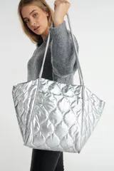Bolso tote plateado, tipo shopper, con diseño acolchado. Forrado internamente en color negro.