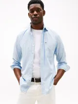 Camisa de hombre Tommy Hilfiger de algodón Oxford elástico, color celeste con rayas verticales finas en blanco y rojo. Tiene corte regular, cuello abotonado, bolsillo de parche en el pecho y logo bordado en el bolsillo.