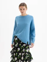 Sweater de punto con textura suave, cuello redondo y mangas largas. Presenta un diseño de silueta relajada con largo por debajo de la cadera y costuras laterales desplazadas hacia el frente, lo que genera un ruedo asimétrico.