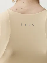 Top deportivo color beige, de cuello redondo con cierre frontal parcial y diseño ajustado.