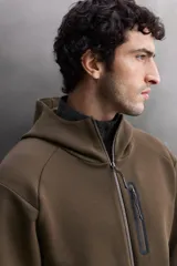 Sudadera con capucha de entrenamiento, confeccionada en tejido técnico de algodón con efecto neopreno. Presenta cierre frontal de cremallera, cuello subido, bolsillos laterales y un bolsillo en el pecho, todos con cierre de cremallera y acabado termofijado.
