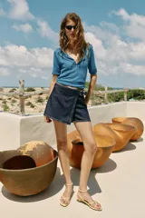 Falda pantalón cruzada de denim en color celeste, con diseño cruzado al frente, cierre frontal oculto y hebilla decorativa redonda en la cintura.