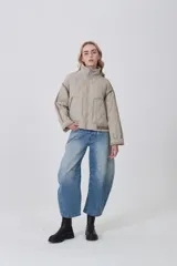 Campera acolchada de diseño capitoné en color beige, con cuello alto, cierre frontal y bolsillos laterales. Presenta un corte holgado con detalles de costuras reforzadas en las mangas y ajuste en la cintura.