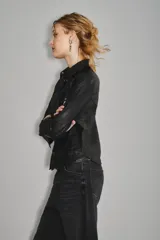 Camisa de cuero ovino con cierre frontal de botones metálicos a presión, cuello clásico y bolsillos delanteros. Presenta un diseño de manga larga con puños abotonados.
