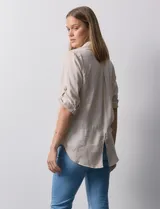 Camisa color beige de tencel, marca Hester & Orchand, con cuello con solapa, escote en V, abertura central con botones y bolsillos delanteros. Las mangas son largas y regulables con presilla y botón.