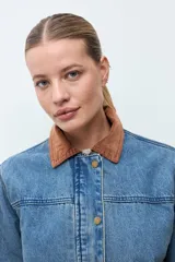 Campera de jean en tono azul medio, con cuello de pana en color marrón, cierre frontal con botones metálicos y bolsillos frontales tipo cargo.