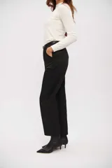 Pantalón negro de vestir, tiro alto, con corte recto y pinzas. Presenta bolsillos laterales y se ajusta con un cinturón fino negro con hebilla metálica plateada.