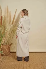 Poleron largo tipo túnica de tejido de punto, color beige, con cuello alto y aberturas laterales. Presenta un diseño holgado y mangas largas.