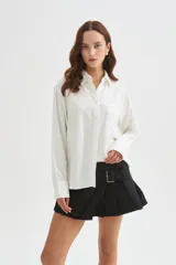 Camisa de viscosa blanca de corte holgado, con mangas largas, cuello camisero, cierre frontal con botones y detalle de bolsillo otonado en el pecho.
