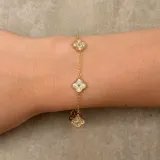 Pulsera de cadena fina dorada con tres dijes en forma de trébol de cuatro hojas, decorados con incrustaciones de cristales brillantes.
