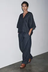 Camisa de tejido tipo denim azul oscuro, con escote pico, manga corta ancha y dos bolsillos de parche frontales. Cierre frontal con botones.