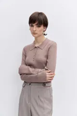 Jersey de punto color beige con cuello polo y cierre frontal de botones. Presenta mangas largas y un ajuste entallado al cuerpo.