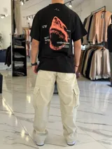 Remera oversize negra con estampa gráfica en la espalda que incluye un tiburón naranja, texto tipográfico y detalles en blanco.