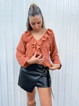 Blusa verde agua con cuello camisero con volados, mangas largas con puños elásticos y corte a la cintura.