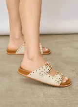 Sandalia chata de gamuza color marrón, con dos tiras cruzadas en el empeine, hebillas de metal dorado y detalles de ojales metálicos a lo largo de las tiras.