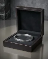 Esclava rígida de acero inoxidable con diseño de tres bandas paralelas y detalle central con piedra de circonia negra flanqueada por pequeñas incrustaciones brillantes.