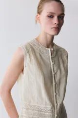 Blusa sin mangas de cuello redondo, confeccionada con detalles de encaje y puntilla a tono. Presenta cierre frontal con botones y diseño estructurado.