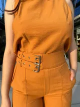 Conjunto de dos piezas color mostaza compuesto por un top sin mangas de cuello redondo y un pantalón de corte recto y tiro alto con cinturón integrado.