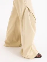 Pantalón wide leg de gabardina color beige, de tiro medio, con recortes diagonales y pespuntes a la vista que aportan volumen, bolsillos delanteros y pasadores en la cintura.