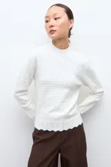 Sweater de punto color crudo con cuello alto tipo media polera, manga larga y diseño con textura de líneas horizontales. Presenta un borde inferior con terminación ondulada.