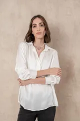Blusa blanca de manga larga con cuello camisero y cierre frontal parcial con botones.