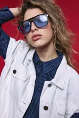 Chaleco de jean color blanco, de corte oversized, con cuello camisero, bolsillos delanteros con solapa y cierre frontal por botones metálicos.