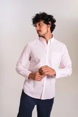 Camisa de manga larga confeccionada en tejido poplin con diseño de rayas verticales finas en color rosado y blanco. Presenta cuello abotonado (button-down), cierre frontal con botones y un bolsillo en el pecho.