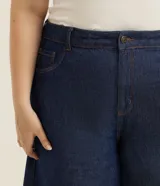 Bermuda tipo jorts de corte amplio y tiro medio, confeccionada en denim de algodón azul oscuro. Presenta diseño de cinco bolsillos, cierre frontal con botón y costuras en tono contrastante.