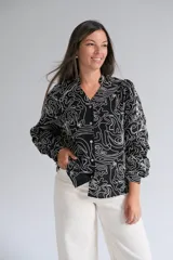 Blusa de manga larga con cuello mao y cierre frontal de botones. Presenta un diseño estampado con líneas blancas abstractas sobre fondo negro.