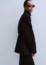 Parka de denim negro de corte largo, con cuello alto, cierre frontal oculto y múltiples bolsillos con solapa en el pecho y los costados. Cuenta con cordón ajustable en la cintura.