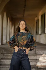 Blusa de lino con estampado artístico en tonos tierra, verdes y azules. Presenta un corte holgado con mangas abullonadas, puños elásticos y un cordón ajustable en el ruedo frontal para entallar la cintura.
