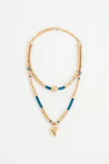 Collar doble de estilo artesanal con cuentas metálicas doradas y cuentas de plástico en color azul petróleo. El diseño presenta un dije central esférico texturizado en la cadena superior y un dije de corazón liso en la cadena inferior.