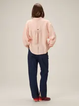 Camisa de lino con cuello camisero, mangas largas con puños y corte holgado. Presenta un canesú trasero con frunces y detalle de pespuntes en zigzag.