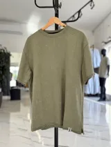 Remera de corte oversize en tejido rústico color verde militar con efecto gastado, cuello redondo ribeteado y dobladillos descosidos.